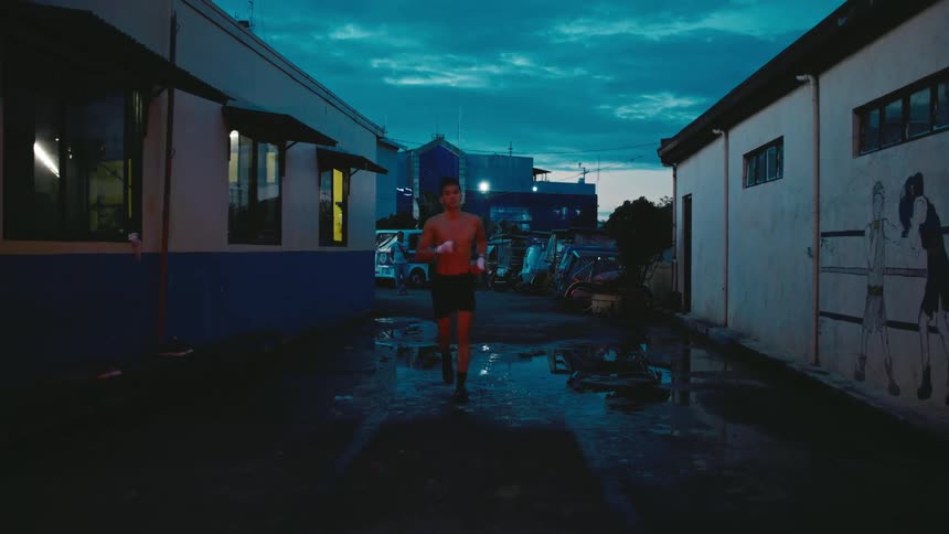 A man with shorts jogging in a alleyway with buildings the sky and clouds in the background