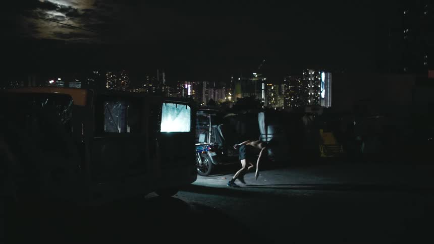 A shirtless man performs dashing exercises in a parking lot in a metropolis at night