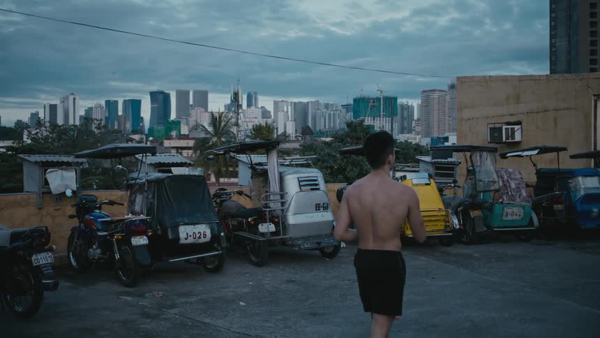 A man with shorts walking with vehicles buildings the sky and clouds in the background