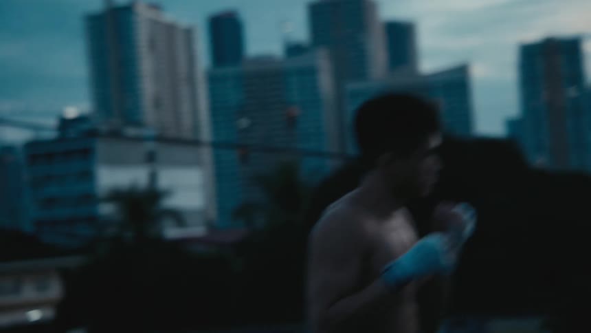 A man shadowboxing on a rooftop with buildings the sky and clouds in the background
