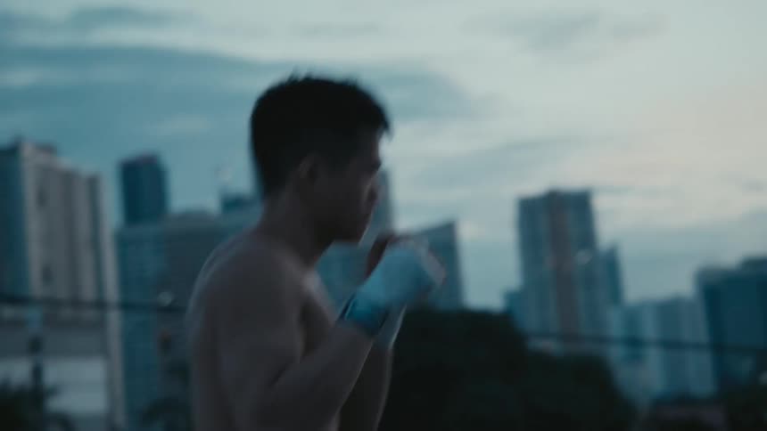 A man shadowboxing with trees buildings the sky and clouds in the background