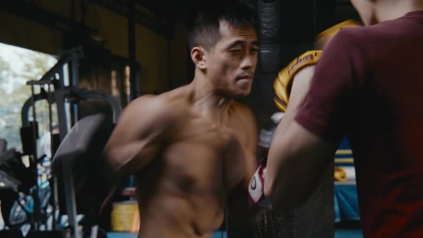 An asian man is practicising boxing with his coach at a gym