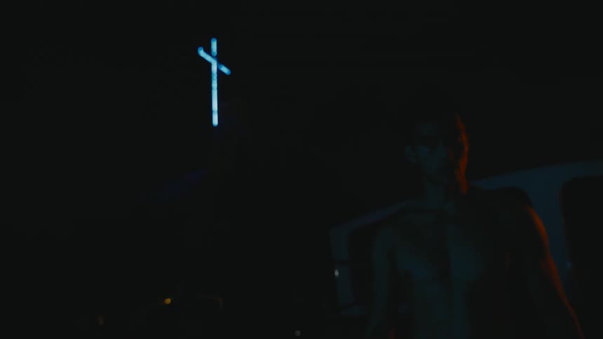 A shirtless man paces in a circle outside a church at night
