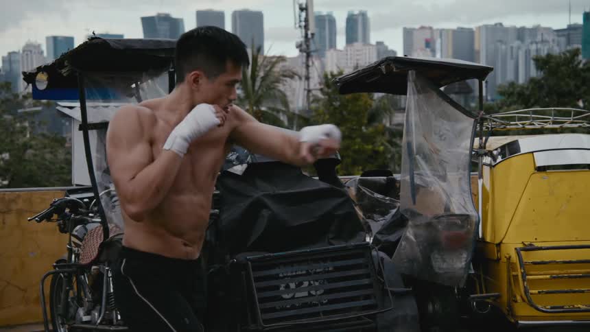 A man on a roof top in a city throws boxing punches