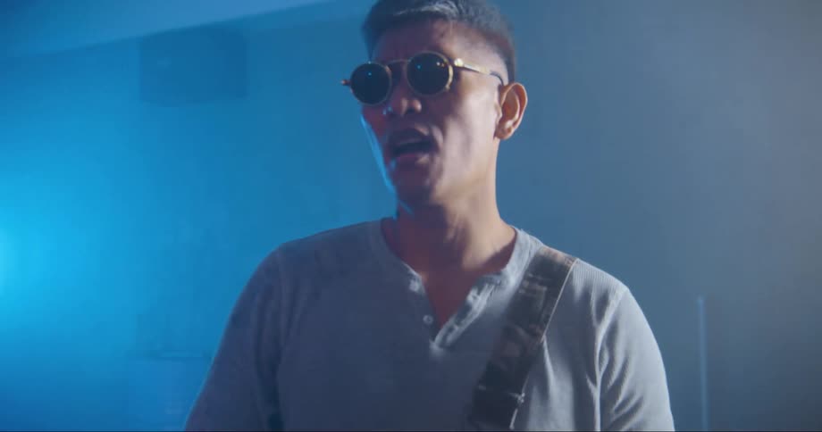 Young asian man wearing sunglasses dancing and singing inside a room filled with smoke