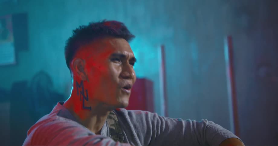 A man in a room singing with a wall and a fan in the background