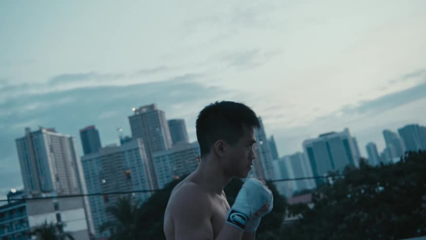 A man throws boxing punches on a rooftop with the city skyline behind him