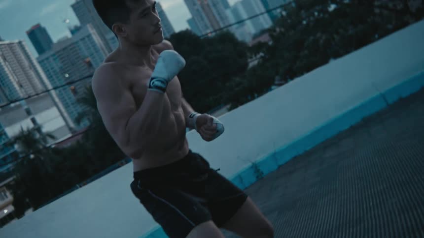Young muscular shirtless man shadow boxing in front of the city skyline at morning