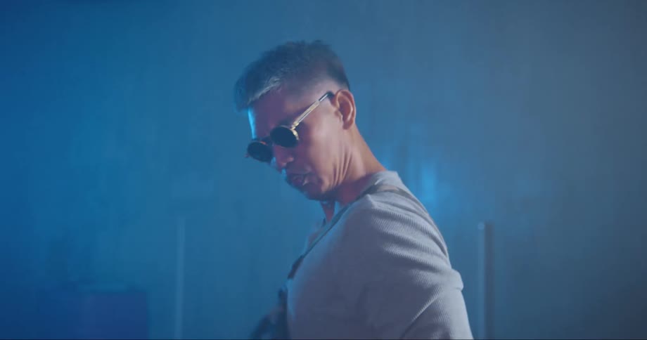 A man with sunglasses dancing in a room with a wall in the background