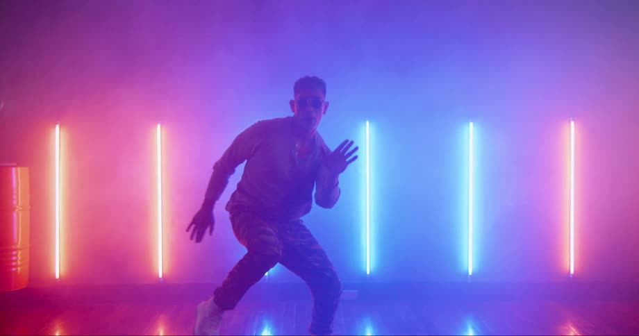 Young asian man dancing inside a room surrounded with colorful neon lights