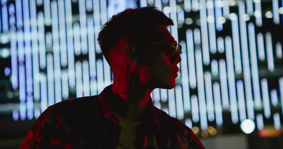 A man stands in front of brightly lit buildings in a city
