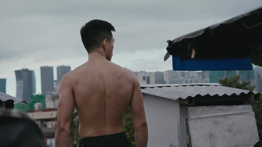 A man is standing outdoors with his shirt off near a downtown city