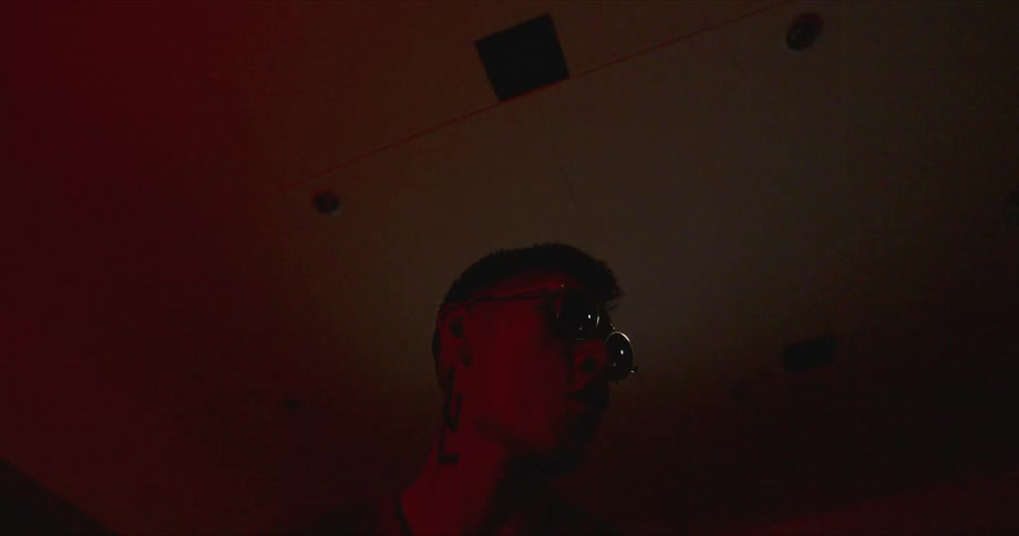 A man with sunglasses in a room with a wall and a light in the background