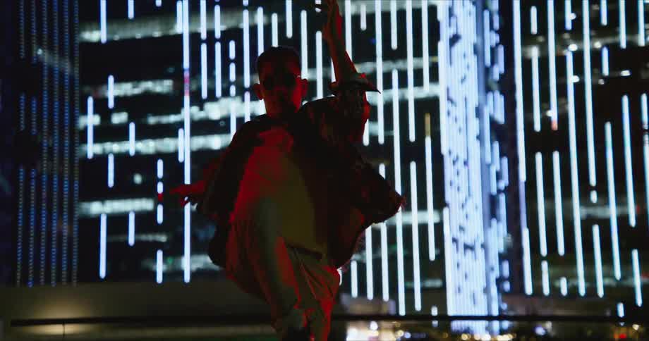 A teenage boy dances outside in front of a lit up high rise building