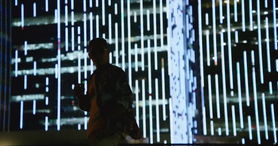 Young asian man wearing sunglasses dances in front of the buildings in the city at night