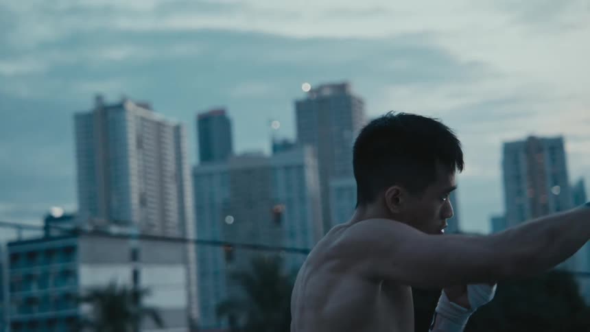 A man is boxing outdoors near a downtown city