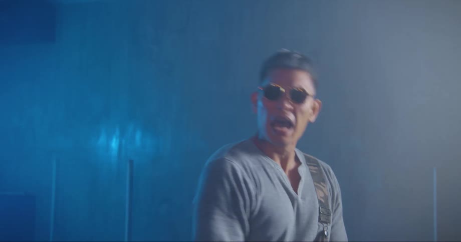 Young asian man wearing sunglasses singing and dancing on a room filled with smoke