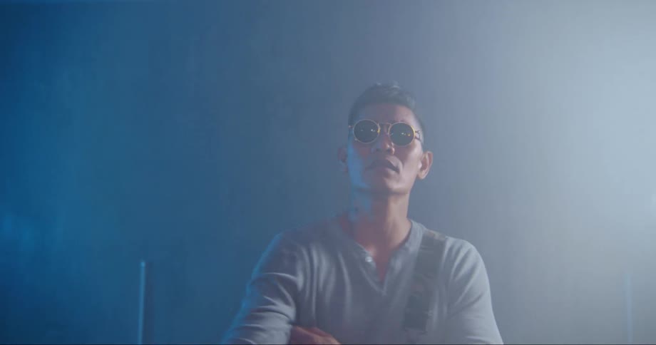 A man with sunglasses in a room singing with a wall in the background