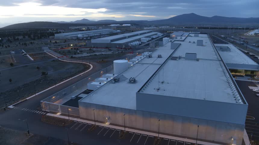 Tilt up pullback reveal of a large data center complex as the sun sets in the distance