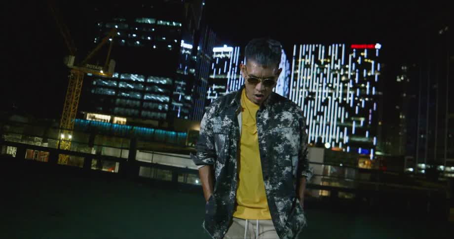 Dancer wearing sunglasses dancing in front of buildings in the city at night while looking at the camera