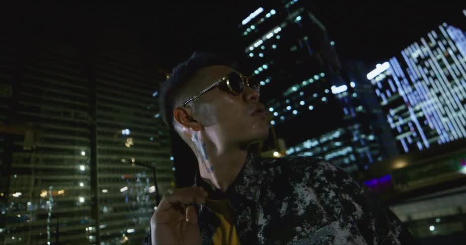 An asian man wearing sunglasses looks at a distance