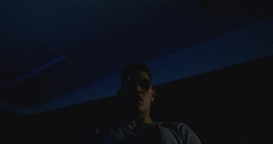 A man with sunglasses in a room with a wall and a light in the background