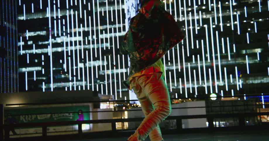 A man with sunglasses dancing with a billboard and buildings in the background