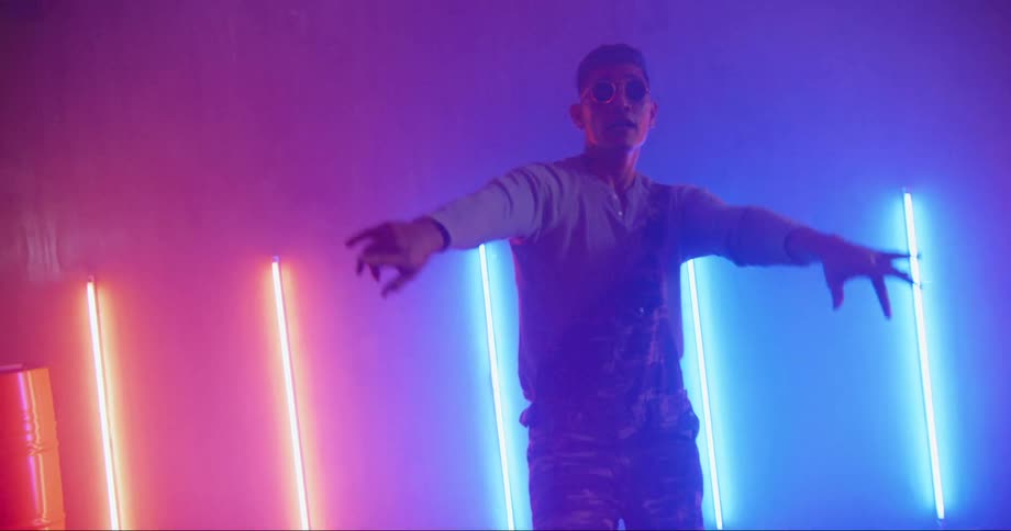 A man in a room with sunglasses dancing with a wall and lights in the background