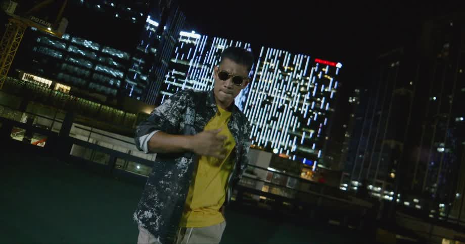 A man with sunglasses dancing on a rooftop with buildings in the background