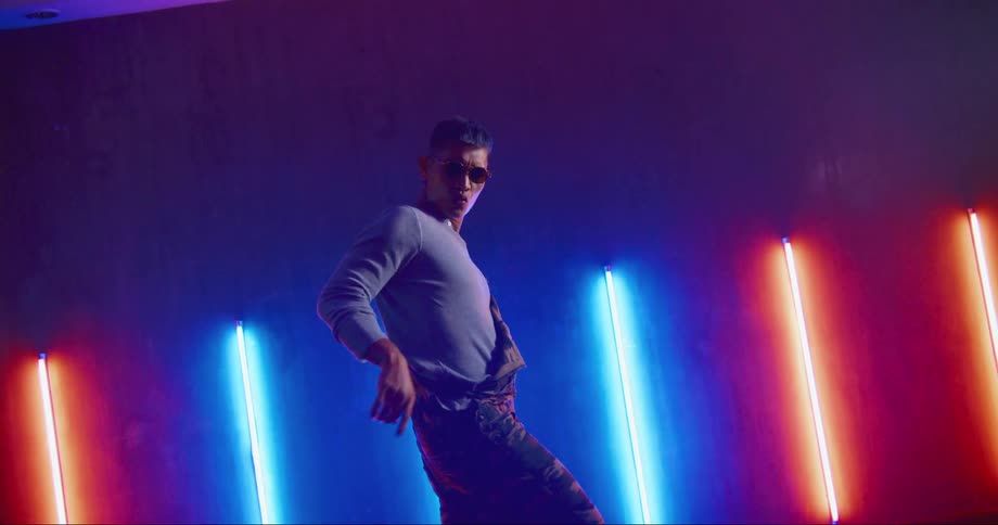 A man with sunglasses dancing in a room with a wall and lights in the background