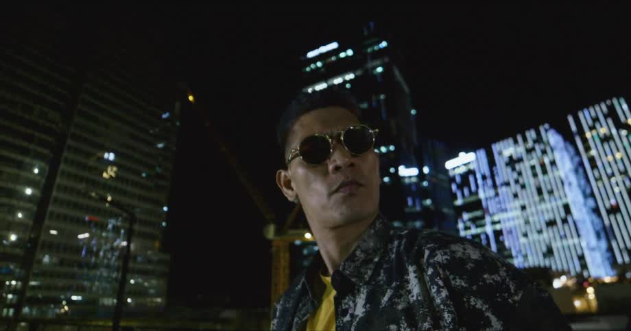 Dancer wearing sunglasses standing in front of buildings in the city at night