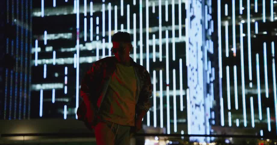 A man with sunglasses dancing on a rooftop with buildings in the background