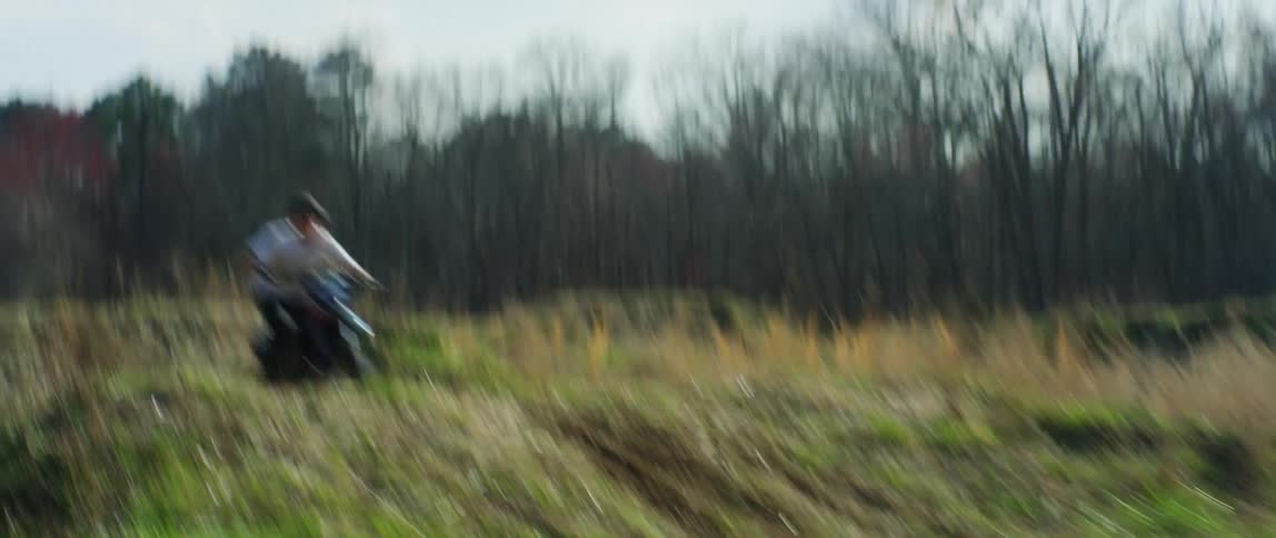 A man rides an offroad motorcycle over dirt ramps in a field on a bright day
