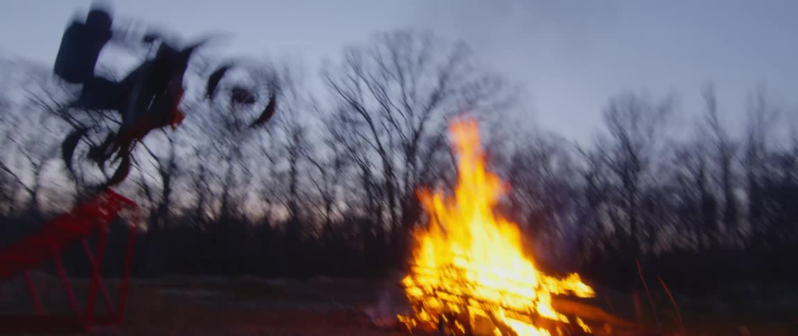 A motorcyclist rides a motorcycle over a ramp and leaps over a bonfire
