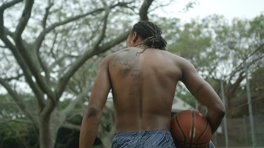 Young shirtless muscular man walking near a tree with a basketball