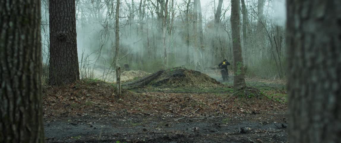 A person rides a motorcycle over a jump in a forest