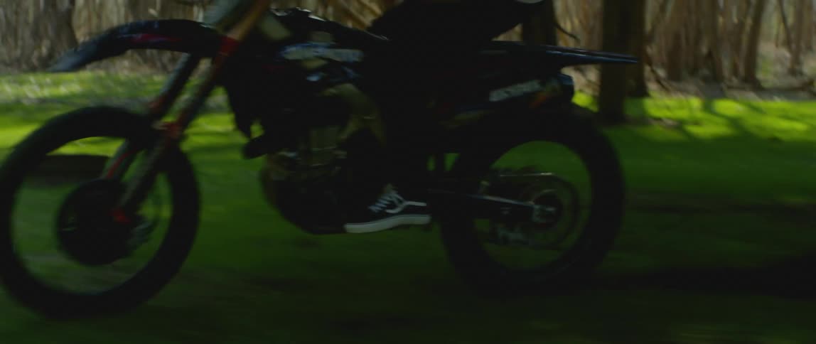 Man rides motorcycle between trees near picnic table