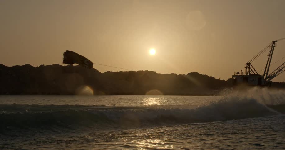 Water skier jumping over the waves on a lake near a construction crane at sunset