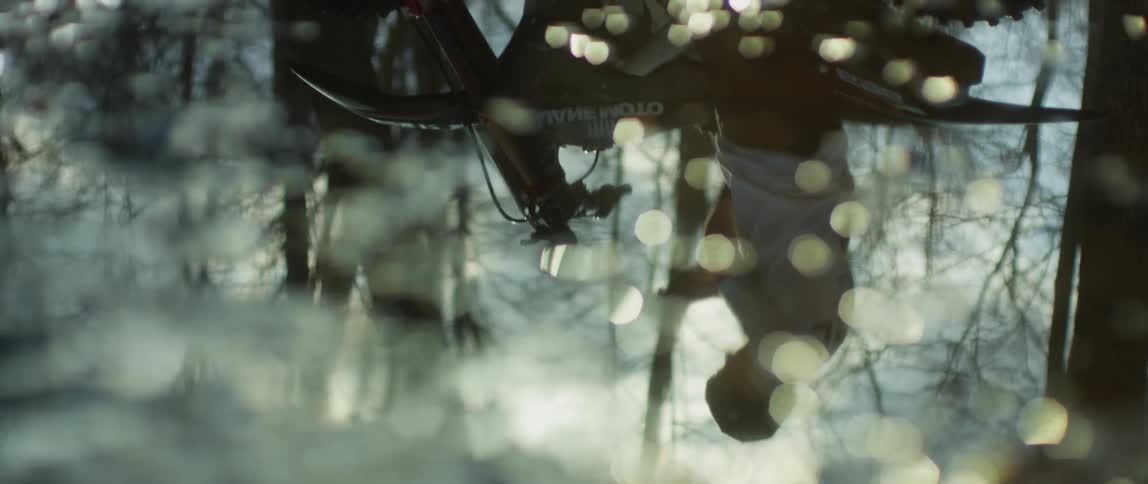 The puddle reflects a man sitting on his dirt bike touching the handlebars