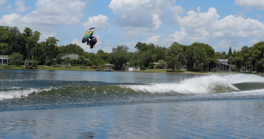 Man riding short board is towed by speedboat and makes tumbling leap in air