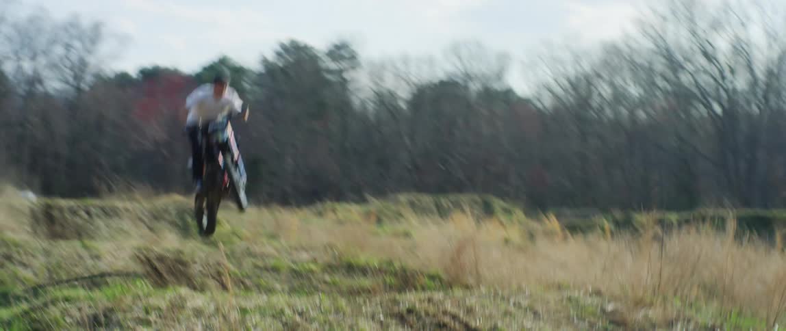 A person driving a motorcycle in a forest with grass and trees