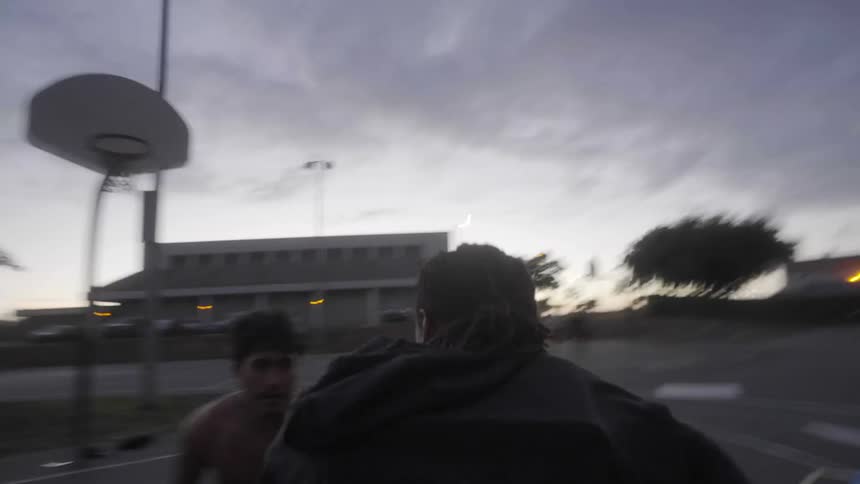 Man dribbling a basketball and scoring a point on an outdoors court at evening