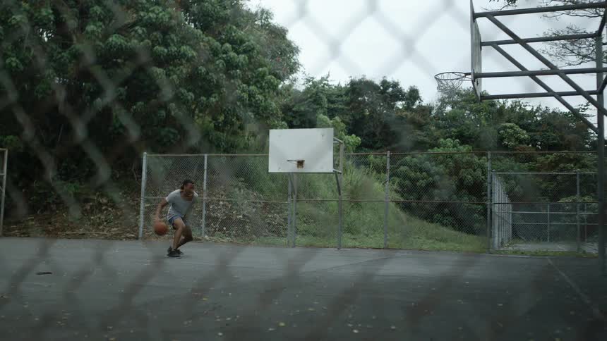 Man with braids a grey t shirt and shorts plays basketball in the basketball court