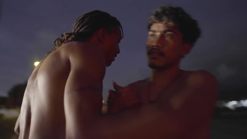 Two men on a basketball court greeting each other with a building the sky and clouds in the background