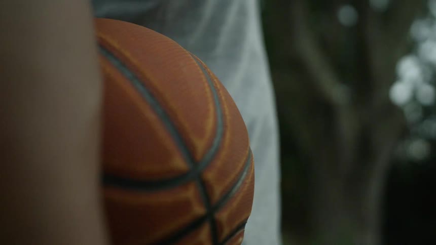 A person is holding a basketball and standing outdoors in spring
