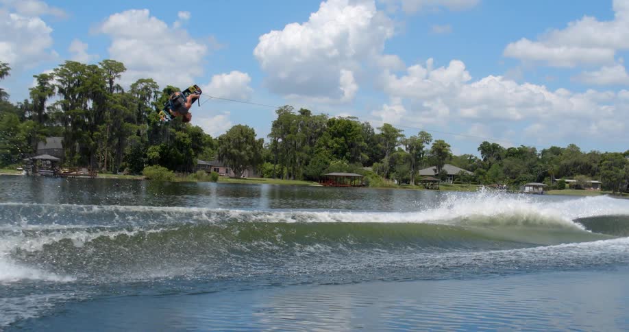 A wakeboader does flips in the air after being sent airborne by waves in the wake of a boat before landing successfully
