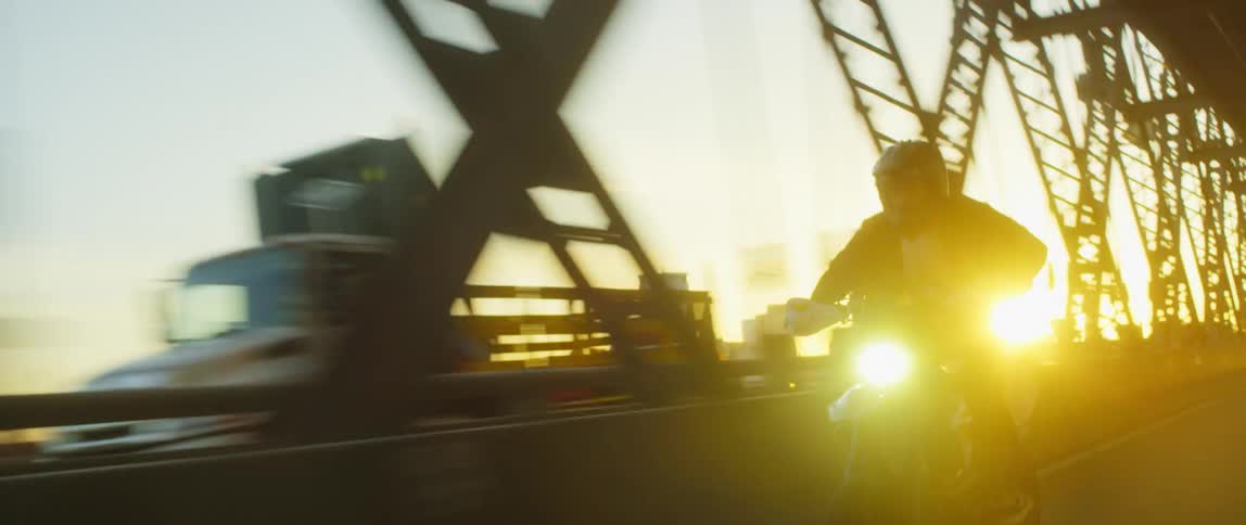 Man riding a motorcycle on a bridge near a city at sunset