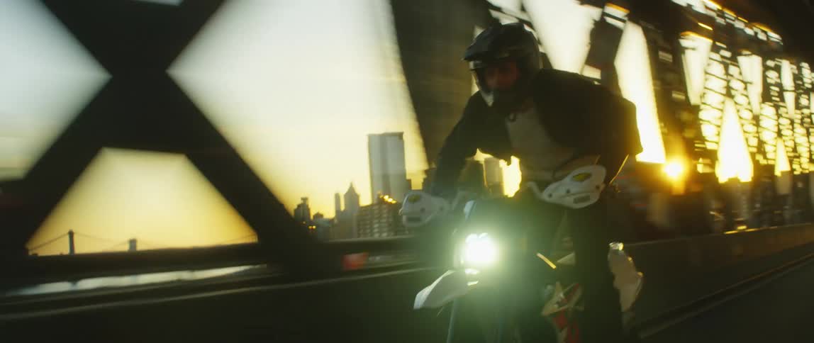 A person with a helmet riding a motorcycle on a bridge with buildings the sky and clouds in the background