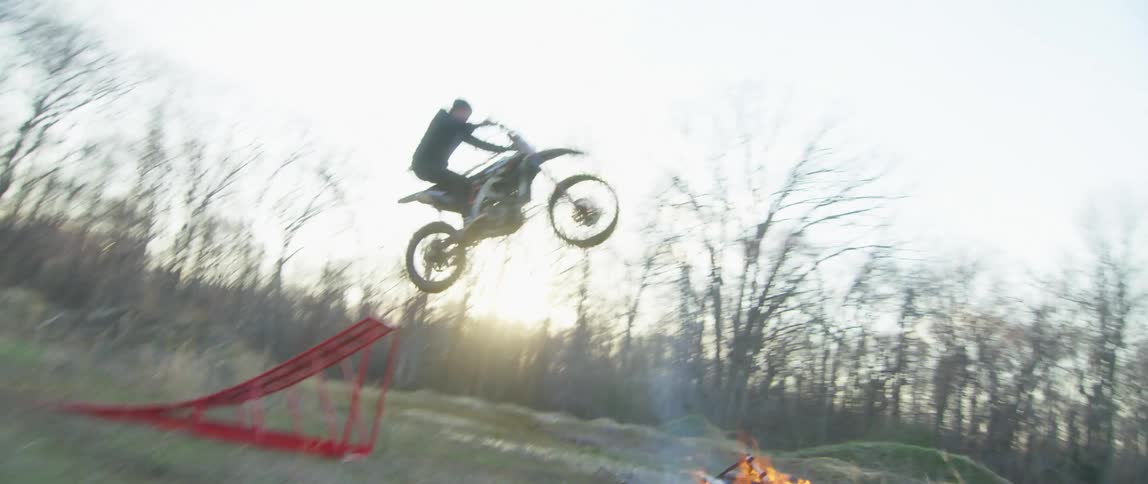 A person riding a motorbike jumps a small fire in a rural field