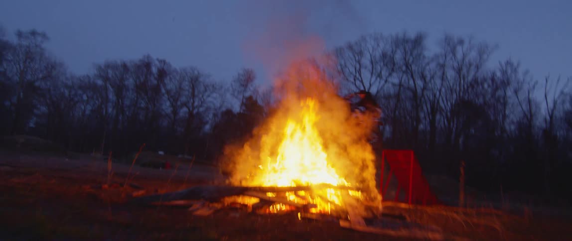 A person riding a motorcycle drives up a ramp and jumps over a large bonfire